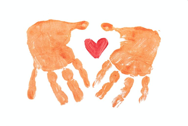 print of a child's two hands using rust-orange paint, with a red heart painted between them