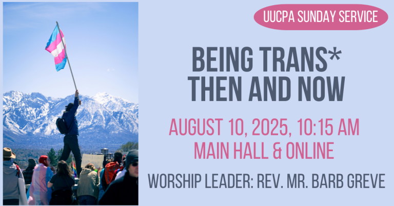 Against a landscape of high, snow-covered mountains, one person stands with a transgender flag held high. Other people, some with pro-trans signs, are gathered in the foreground near the person.